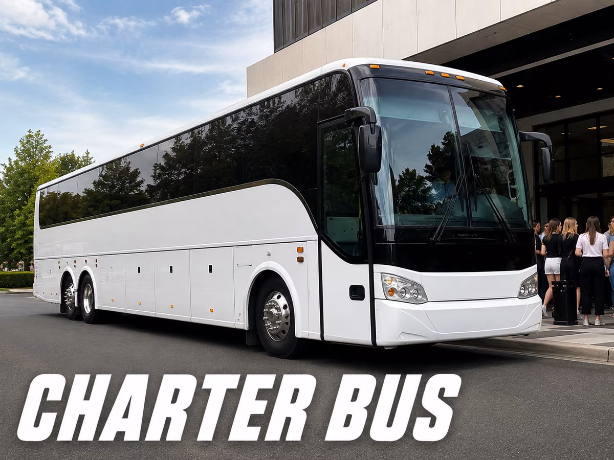 White charter bus at a building entrance with a group of passengers and luggage waiting to board