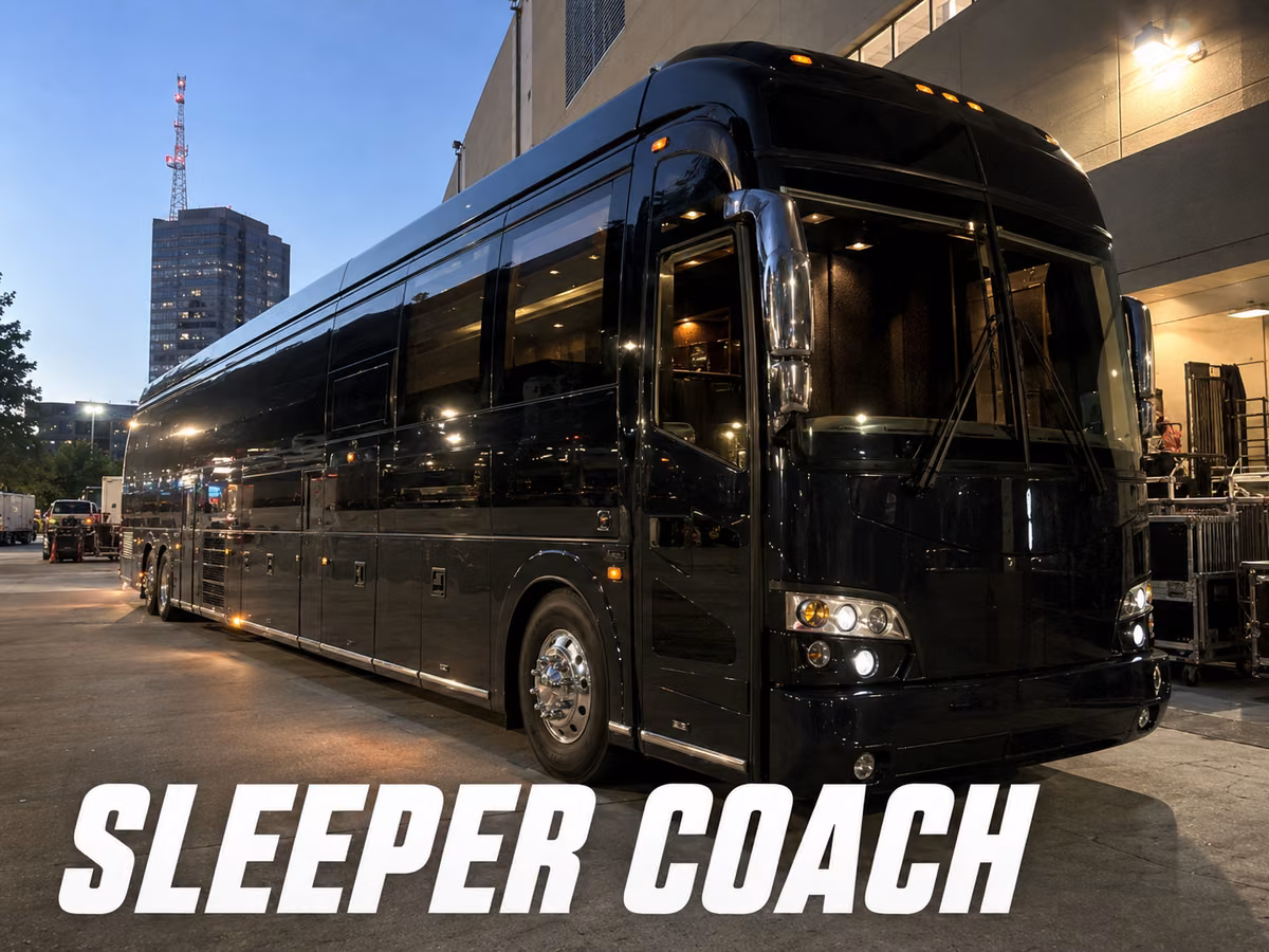 Black entertainer sleeper coach parked at a loading dock at dusk beside road cases