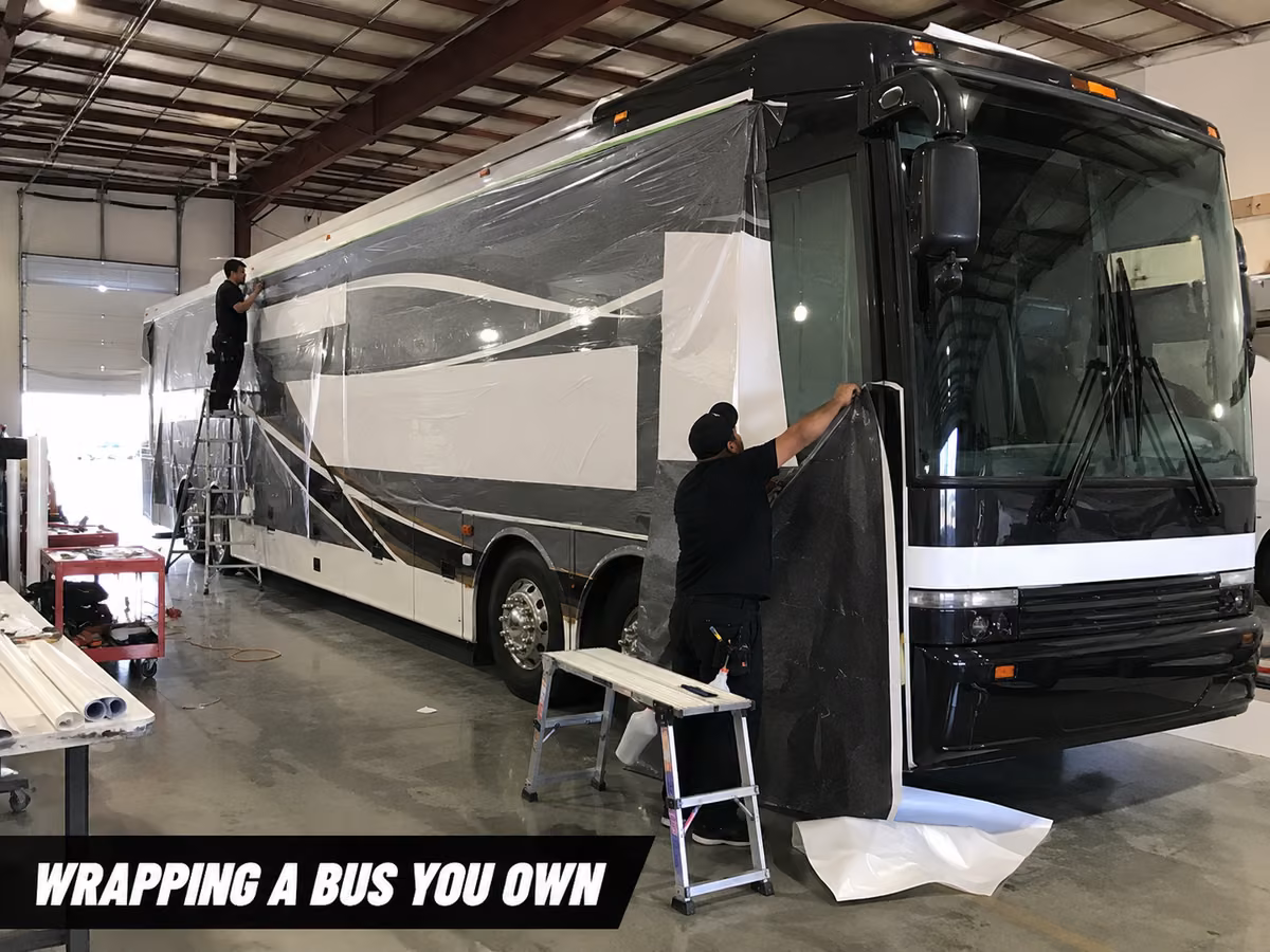 Installer working on vinyl film beside a bus with a stepladder