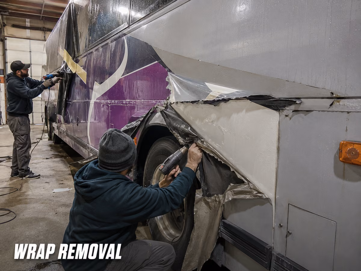 Worker peeling old vinyl film from the lower panel of a bus