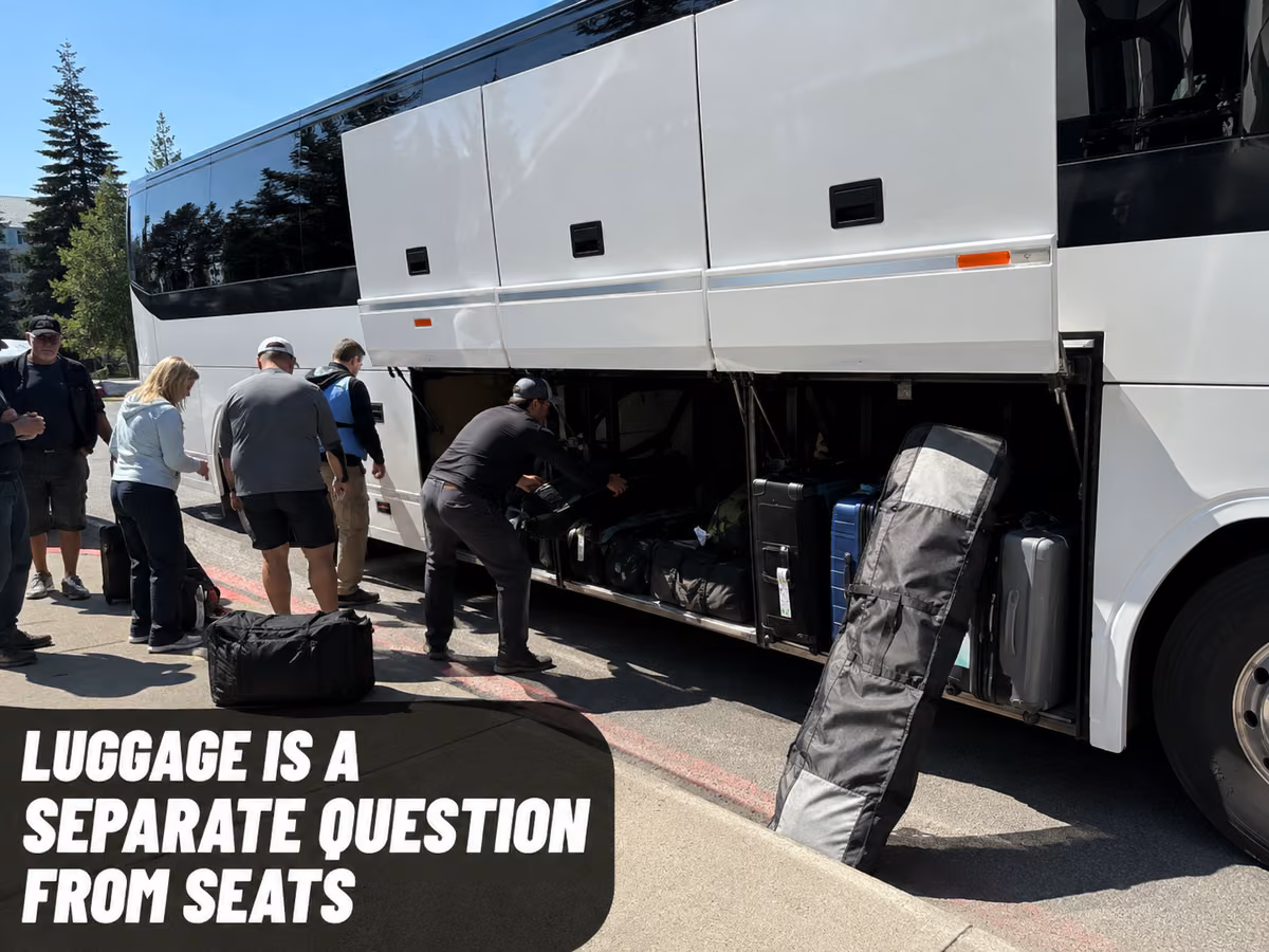 People loading suitcases into the open underfloor luggage bay of a white full-size coach.