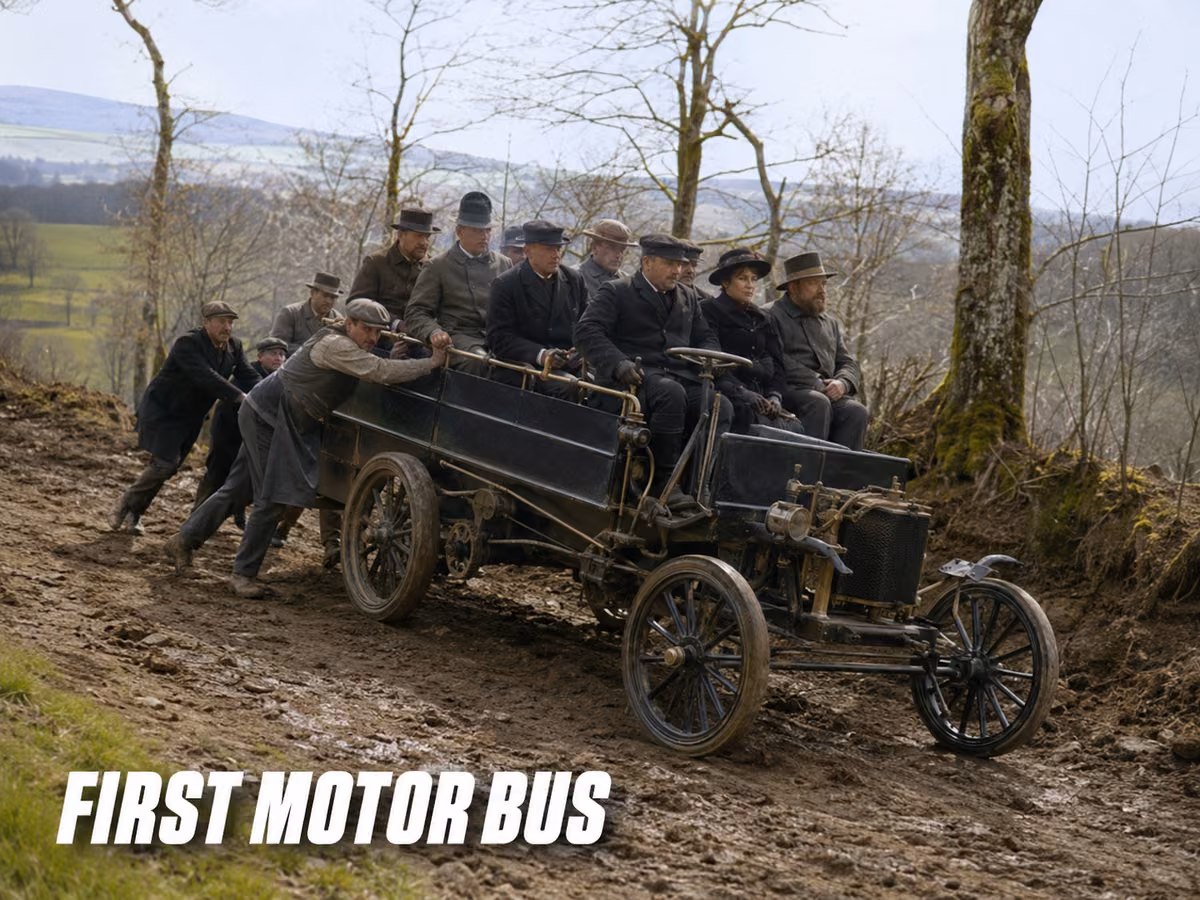 Men in period clothing pushing an early open motor bus up a muddy hillside