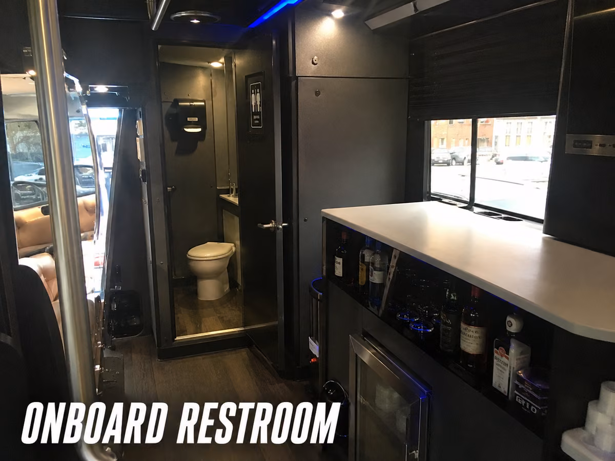 Interior of a party bus showing an onboard restroom beside a bar area