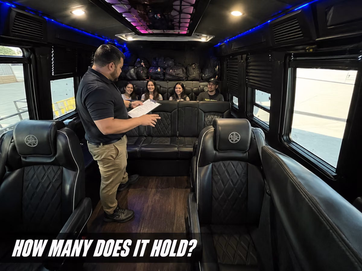 A man with a clipboard standing inside a party bus showing details to passengers seated along the leather bench