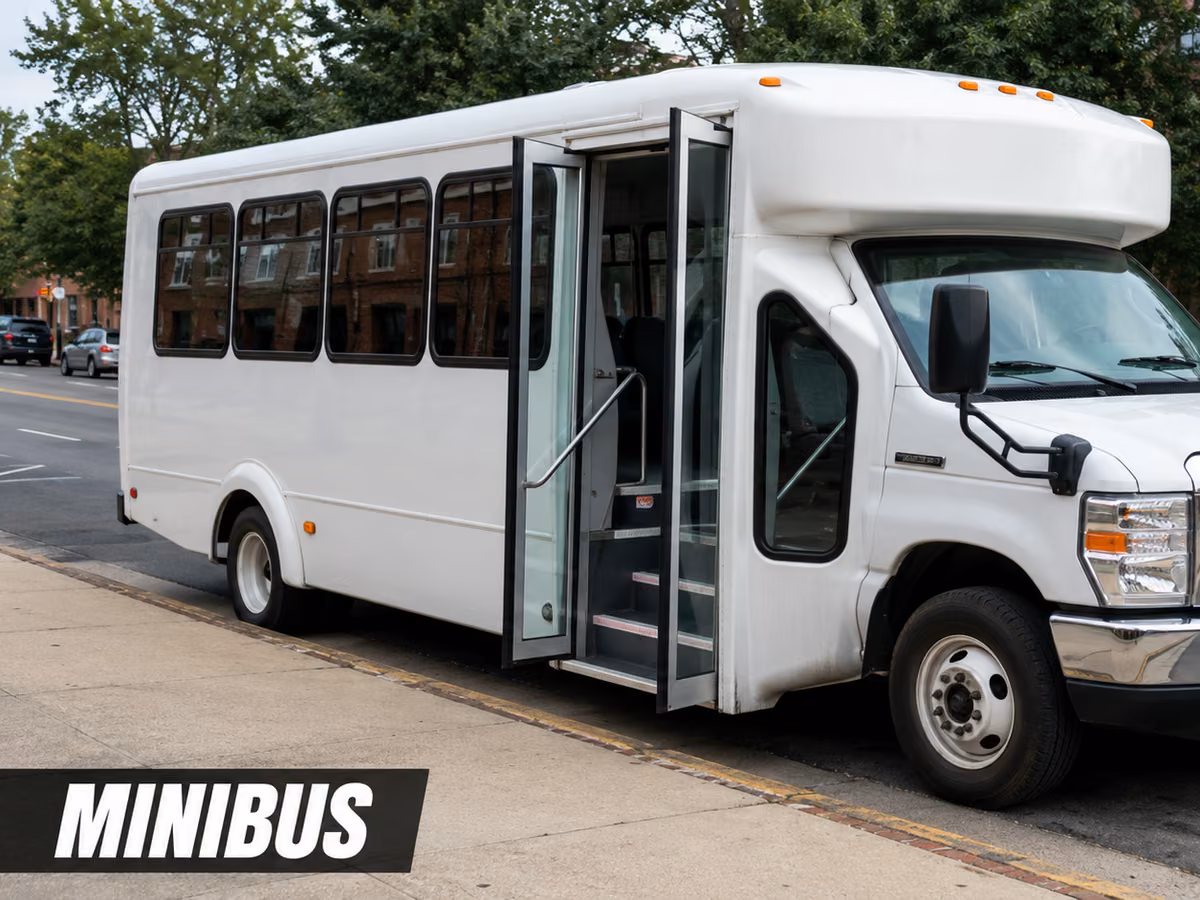 White minibus parked at the curb on a city street, seen from the front and side.