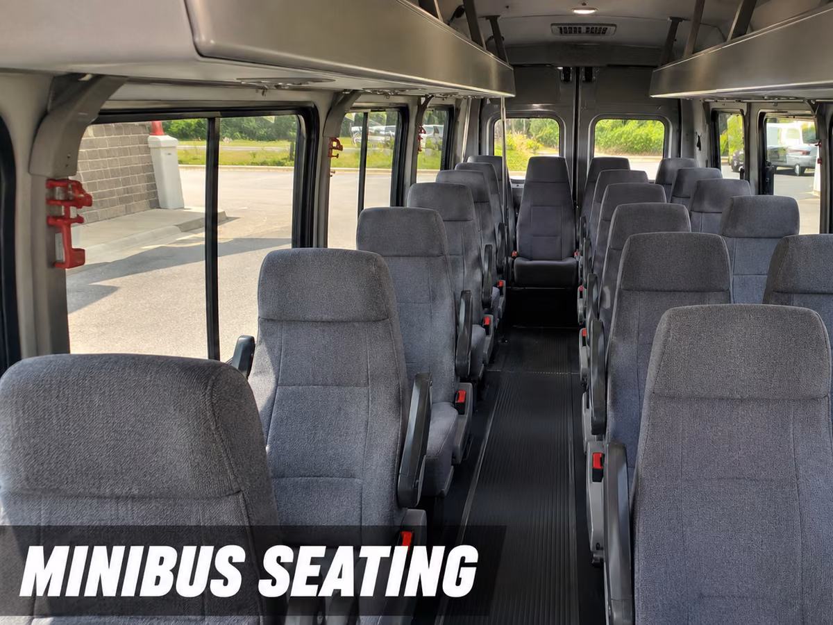 Interior of a minibus showing rows of gray cloth seats along a center aisle.