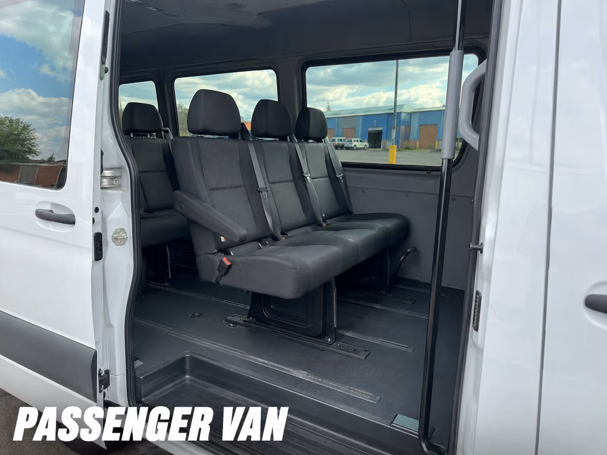 White Mercedes-Benz Sprinter passenger van with its side door open, showing rows of gray cloth bench seats.